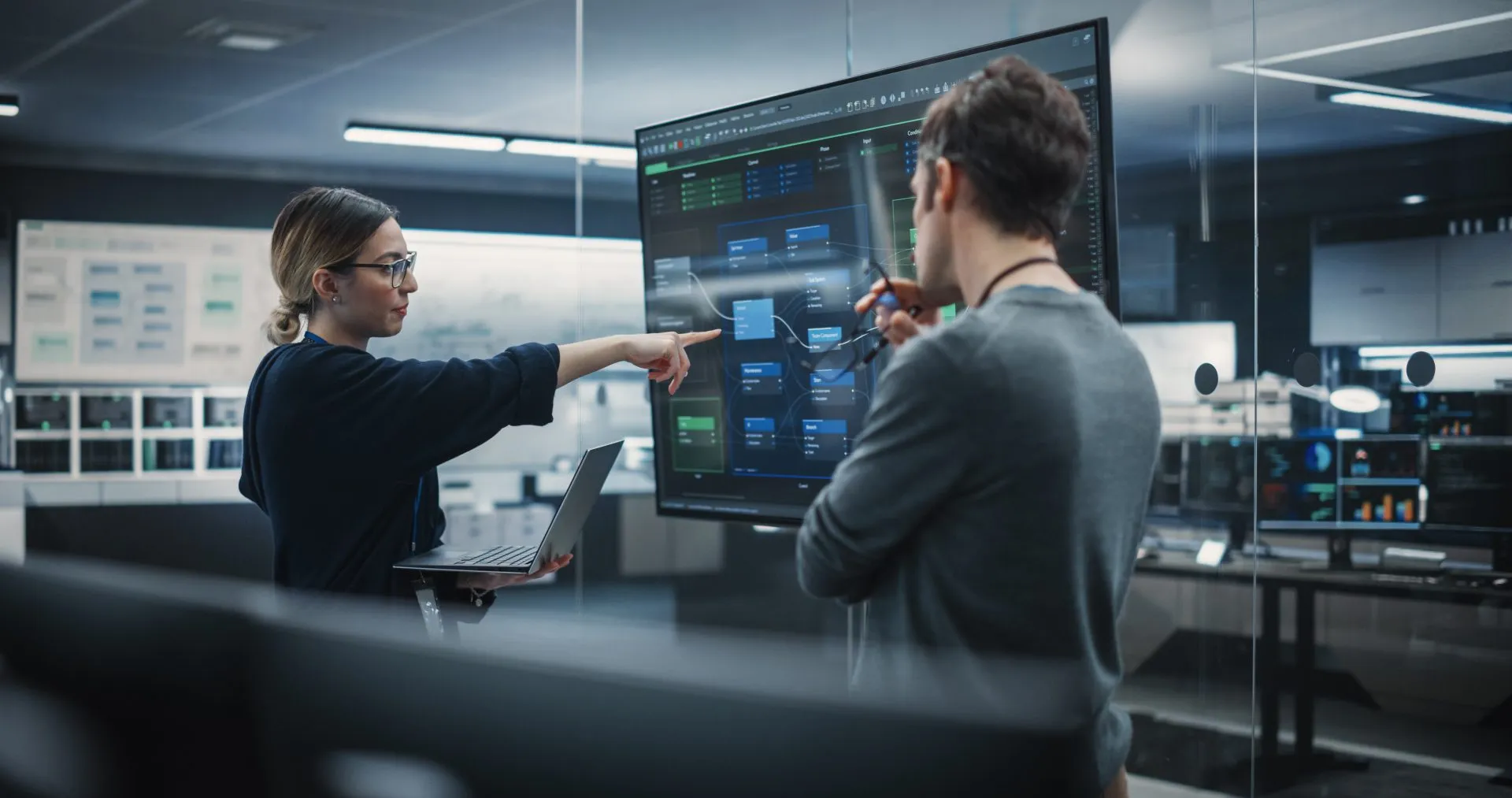 Two people analyzing data on large digital screens in a modern control room.